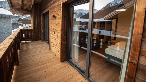 Un balcon en bois doté d’un plancher en bois et de portes vitrées donnant sur une pièce offrant une vue sur les montagnes.
