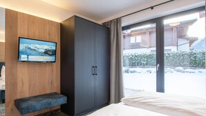 Une chambre d’hôtel moderne dotée d’un grand lit, d’un coin salon, d’une armoire et d’un téléviseur diffusant des images d’un paysage enneigé.