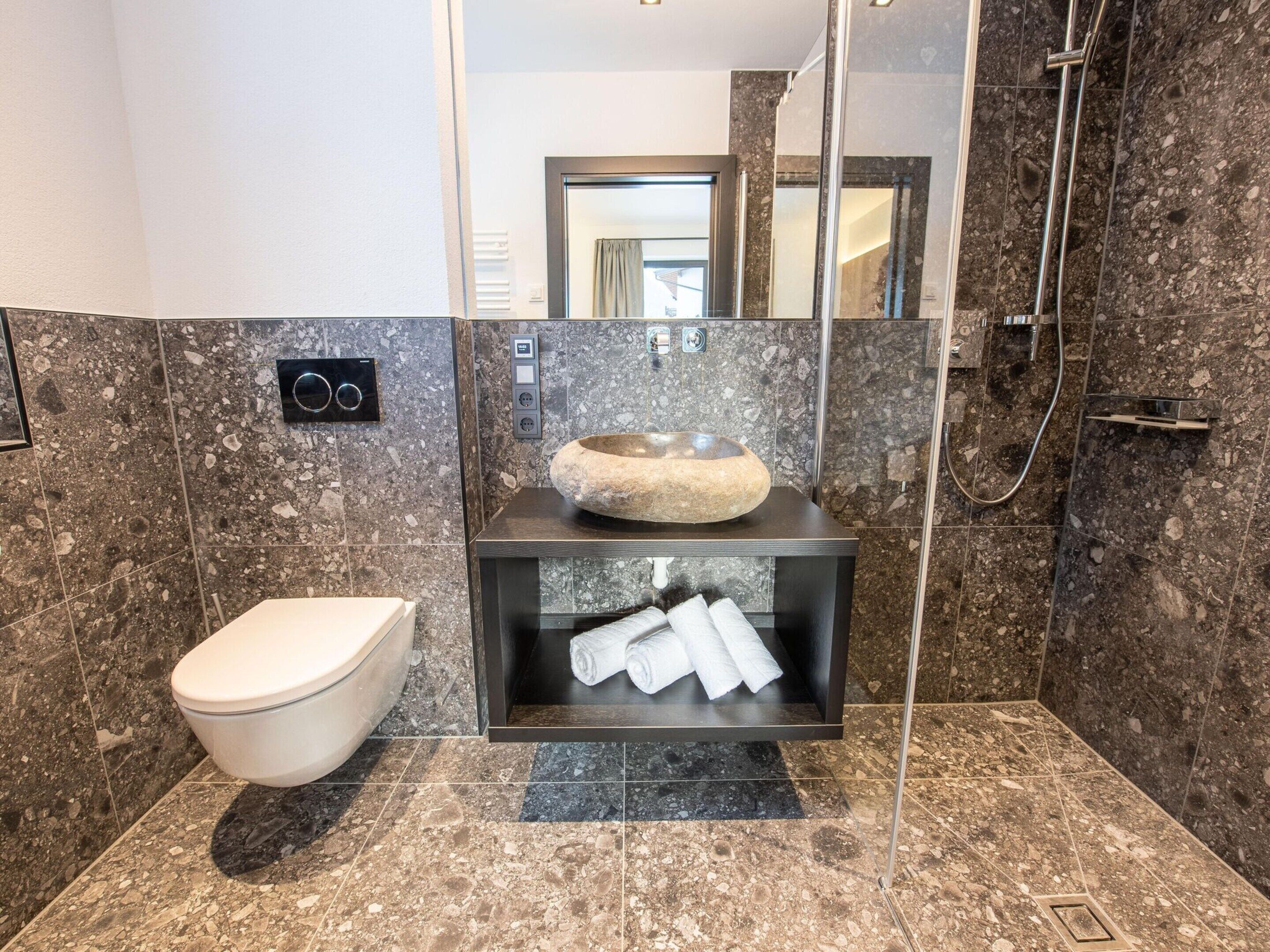 A modern bathroom with a toilet, a stone sink, and a glass-enclosed shower area.