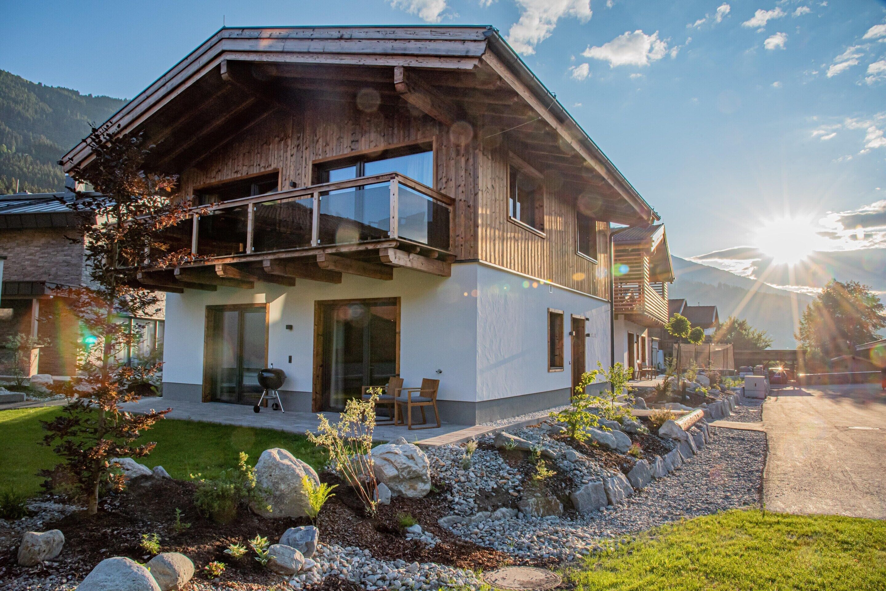A modern two-story house with a balcony, large windows, and a stone foundation.