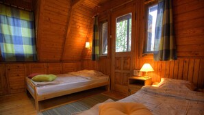 Een knus vakantiehuisje met twee houten bedden, een eettafeltje en een raam met gordijnen.