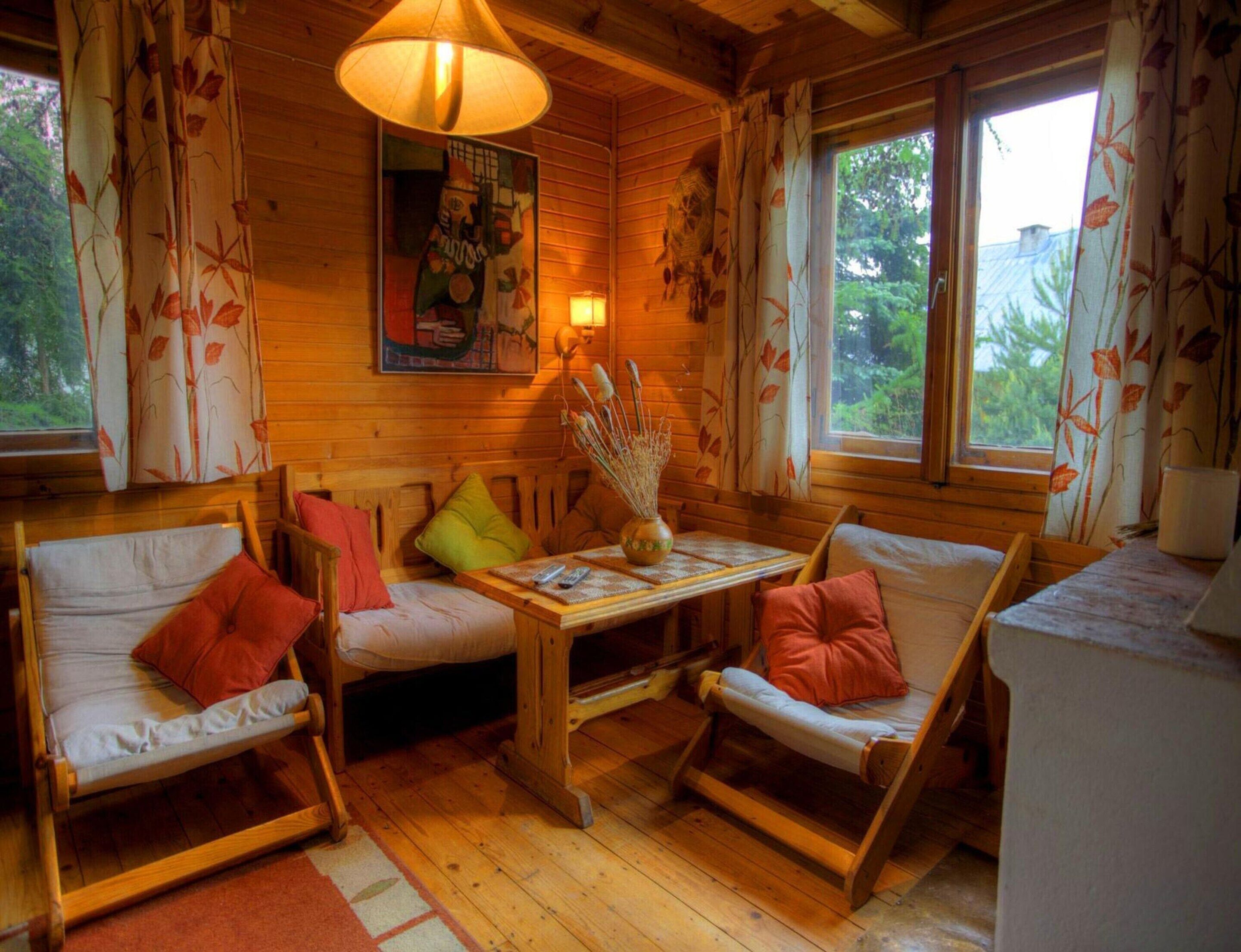 A cozy cabin interior with wooden walls, a dining table, two sofas, and a window with curtains.
