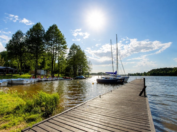 A wooden dock extending into calm water with boats moored on the left, surrounded by trees and a clear sky. - Log House by Lake Tajty, Masurian Lakes Trail (Gizycko)