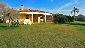 Une maison à deux étages, avec un toit en tuiles, une terrasse couverte et une pelouse bien entretenue.