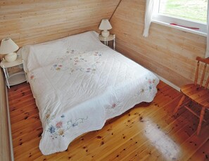 A bedroom with a wooden floor, a bed with a floral bedspread, two bedside lamps, and a window with curtains. - Holiday Home on Lake Ostrowo Near Baltic Sea (gmina Wolin)