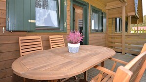 A wooden cabin with a round wooden table and chairs, a potted plant, and green shutters on the windows. - Holiday Home Near Dabki Beach (Darlowo)