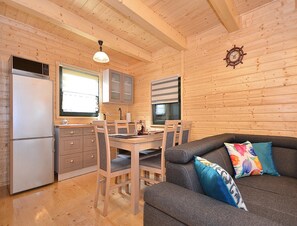 A cozy cabin interior with a dining area, kitchen, and a sofa with floral cushions. - Holiday Home Near Dabki Beach (Darlowo)