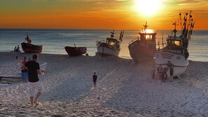 Boats docked on a beach with the sun setting in the background. - Holiday Home Near Dabki Beach (Darlowo)