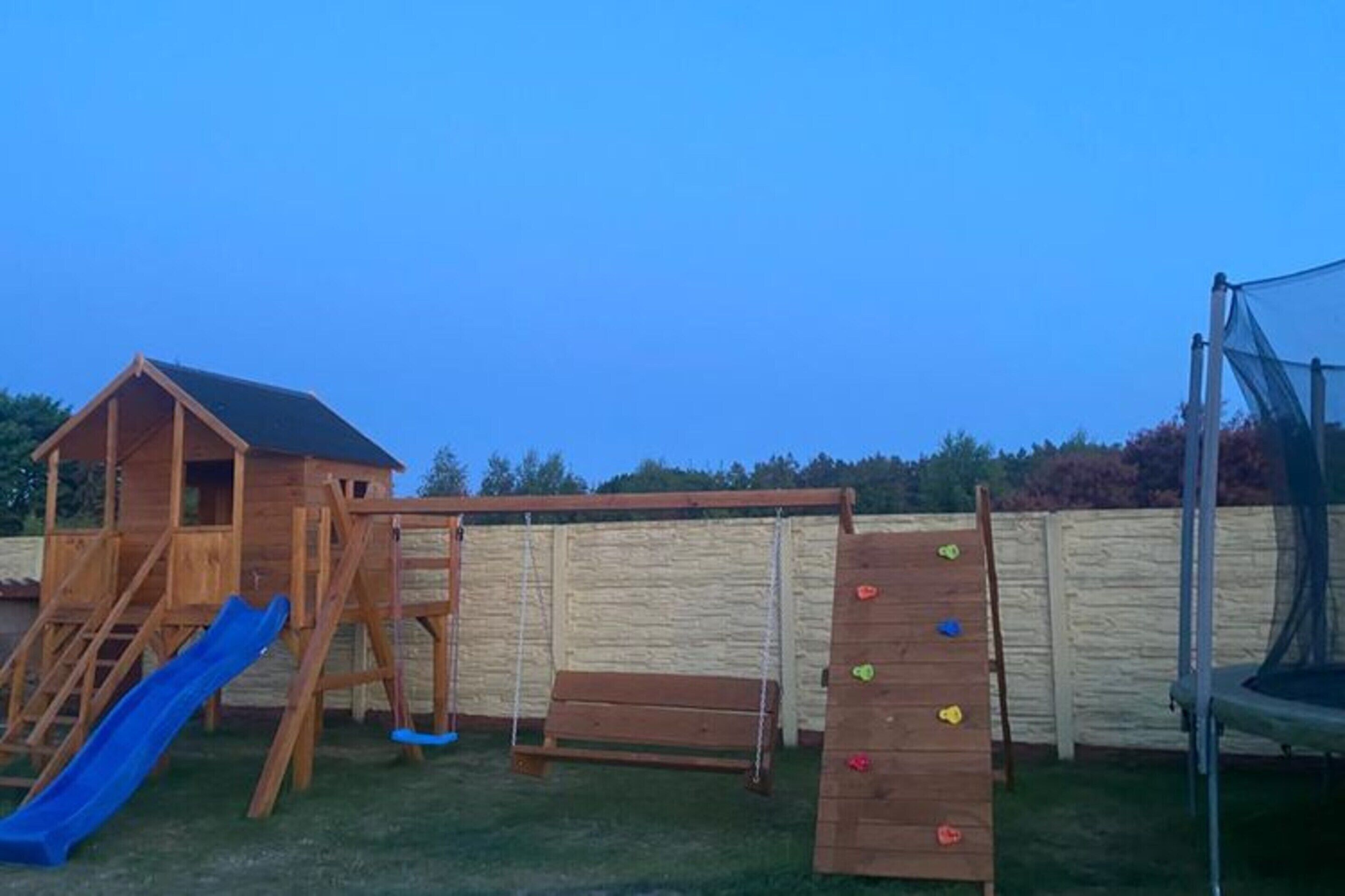 Eine hölzerne Spielanlage mit Rutsche, Kletterwand und Schaukel im Garten.
