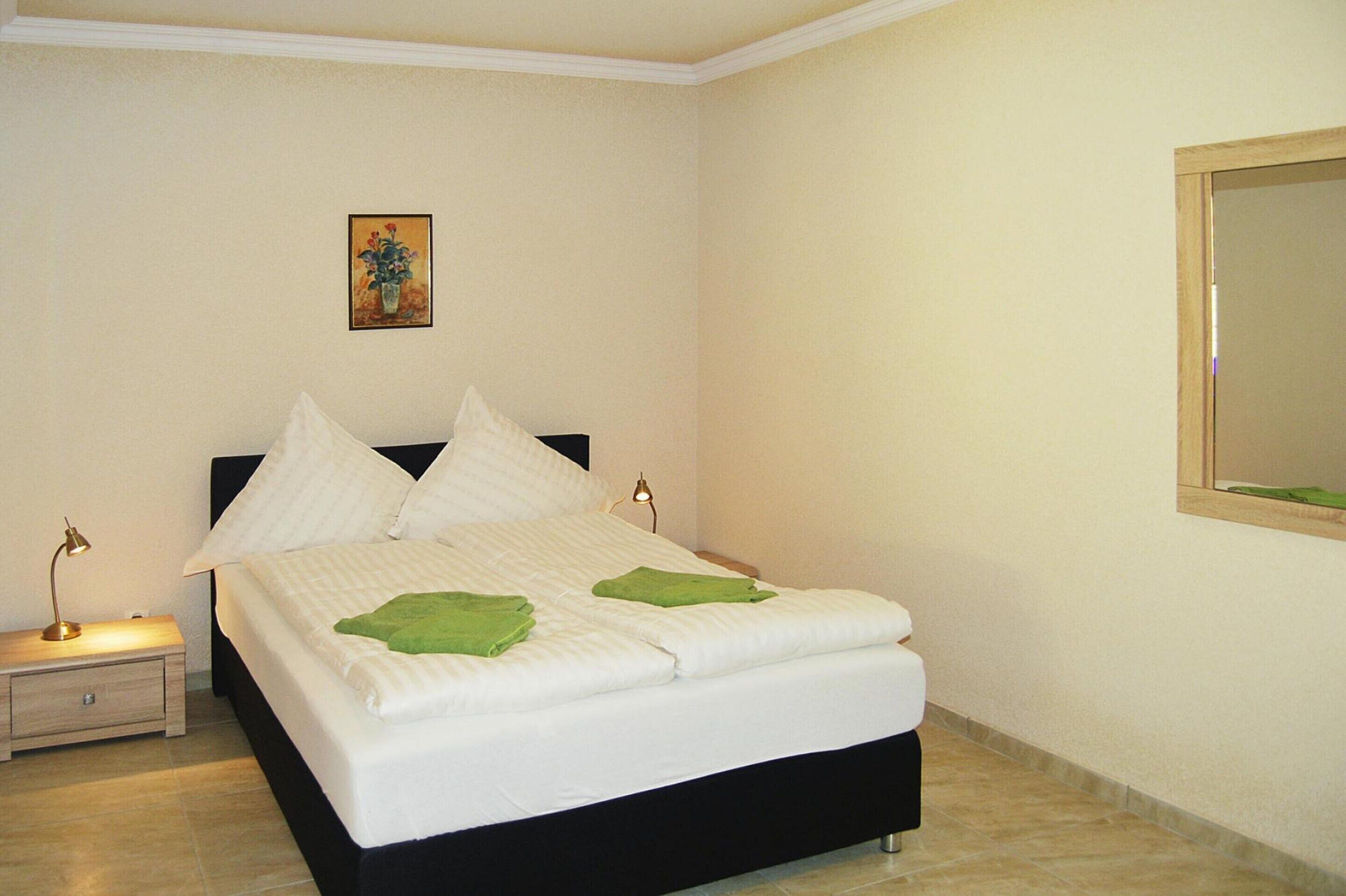 A neatly made bed with white linens and green towels, a bedside lamp, and a painting on the wall.