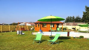 A backyard with a wooden playhouse, a swing set, a pool, and two green lawn chairs. - Large Holiday Villa With Summer Pool and Sauna (gmina Sianów)