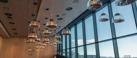 Un intérieur moderne agrémenté de luminaires suspendus, de bancs en bois et de grandes fenêtres offrant une vue sur un téléphérique.