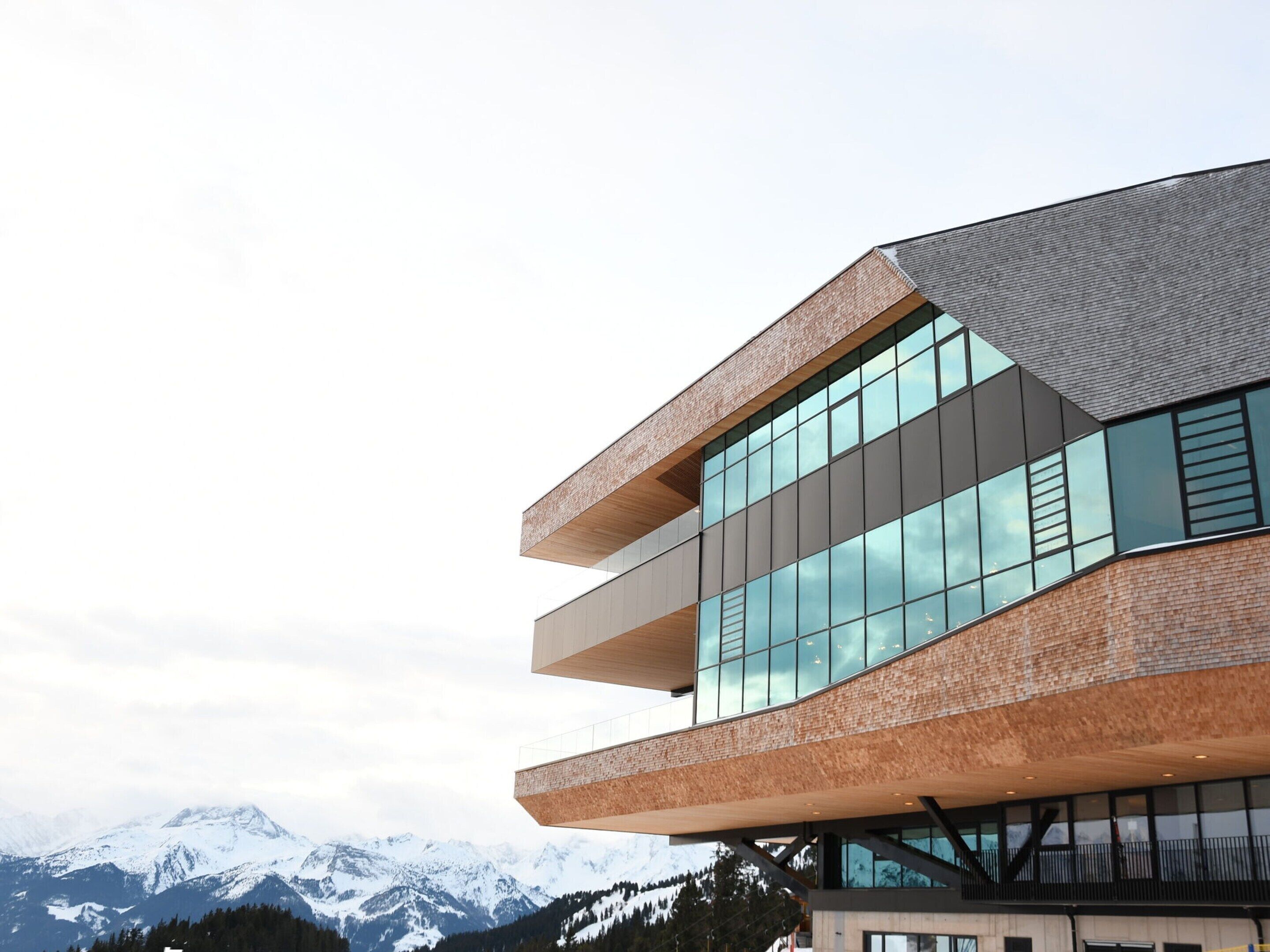 A modern building with a unique angular design, large windows, and a view of snow-capped mountains in the background.
