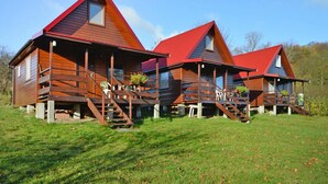 A row of wooden cabins with red roofs, each featuring a balcony and a staircase leading to the entrance. - Wooden House in Lubin by Lake Wicko (Międzyzdroje)