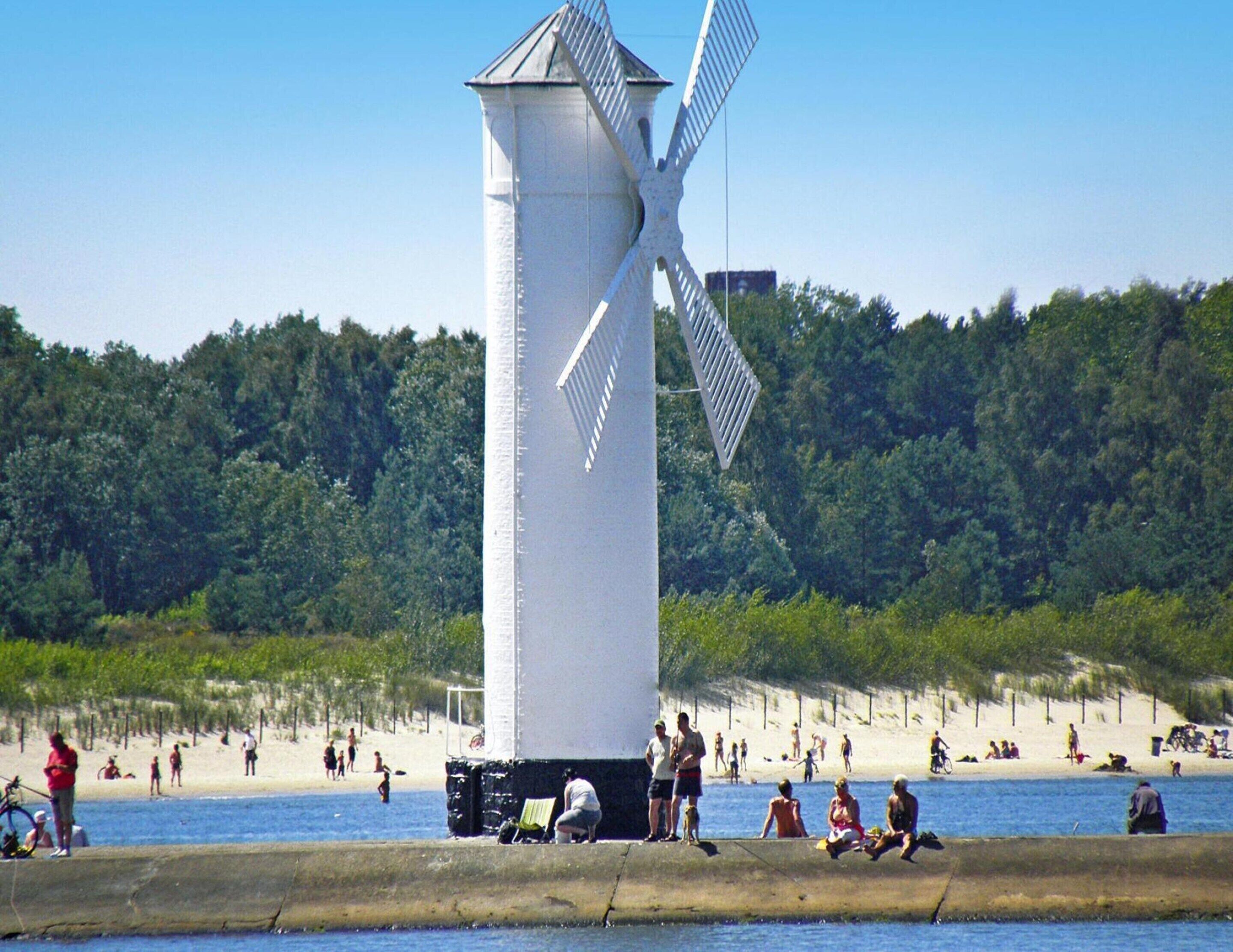 A windmill near a beach with people and a sandy shore.