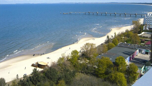 A beach with a pier extending into the water, buildings along the shore, and a clear sky. - Wooden House in Lubin by Lake Wicko (Międzyzdroje)