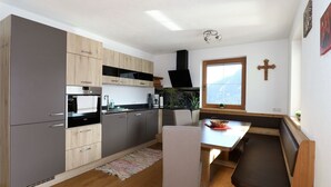 A modern kitchen with grey cabinets, a wooden dining table, and a bench. - Apartment in Fugenberg Near Spieljochbahn (Fuegenberg)