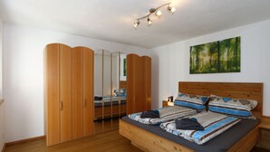 A bedroom with a wooden bed, a wardrobe with mirrors, and a painting on the wall. - Apartment in Fugenberg Near Spieljochbahn (Fuegenberg)