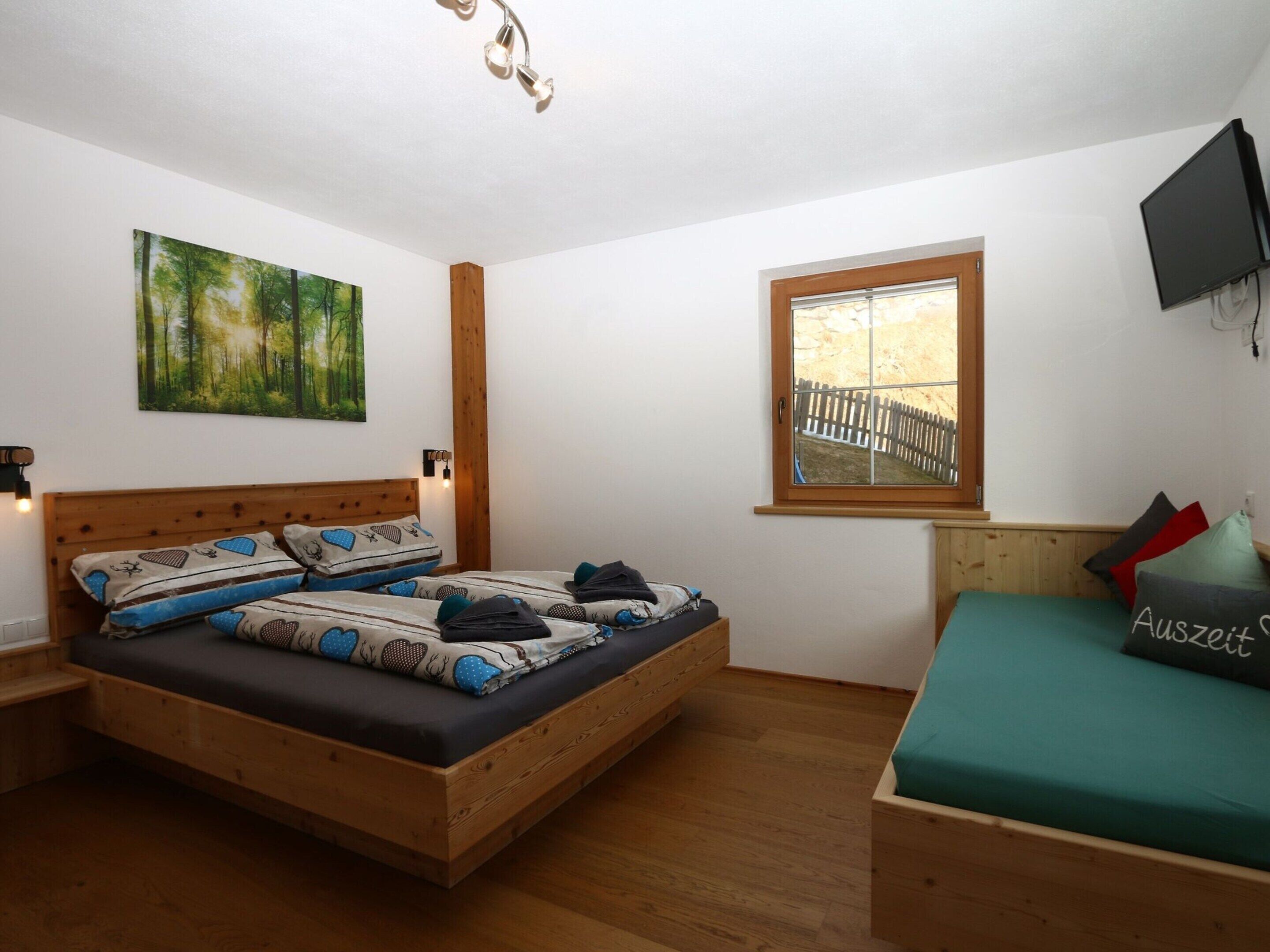 Ein Schlafzimmer mit einem hölzernen Bett, einem Fenster mit Blick, einem Bild an der Wand und einem Fernseher an der Wand.