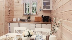 A cozy wooden cabin with a kitchen area featuring a dining table set with a cup, flowers, and a decorative item. - Blue Lagoon - Vacation Home in Nowe Warpno (Nowe Warpno)