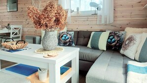 A cozy living room with a white table, a grey sofa with blue and white cushions, and a vase with dried flowers. - Blue Lagoon - Vacation Home in Nowe Warpno (Nowe Warpno)