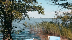 Two blue lounge chairs with woven cushions by a lake, surrounded by trees and reeds. - Blue Lagoon - Vacation Home in Nowe Warpno (Nowe Warpno)