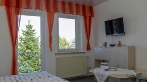A bedroom with a bed, a desk, a television, and a window with curtains. - Ferienwohnung Basteiblick in Pirna (Pirna)