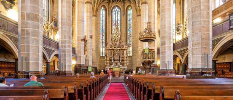 Interior de iglesia con altos techos abovedados, vidrieras de colores y hileras de bancas de madera.
