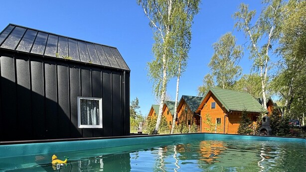 A swimming pool with a yellow duck, surrounded by wooden cabins with green roofs and tall trees. - Bungalow in Dziwnow Near Baltic Sea (Dziwnów)
