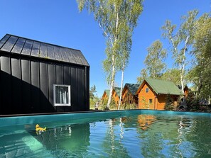 Une piscine avec un canard jaune, entourée de cabanes en bois aux toits verts et de grands arbres.