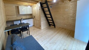 A compact room with wooden walls and a sloped ceiling, featuring a kitchenette, a dining area with a table and chairs, and a ladder for access to the upper level. - Bungalow in Dziwnow Near Baltic Sea (Dziwnów)