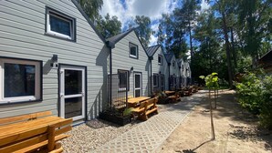 A row of cabins with sliding doors, wooden benches, and a gravel pathway. - Bungalow in Dziwnow Near Baltic Sea (Dziwnów)