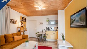 A compact living space with a wooden ceiling, a kitchenette, a sofa, a dining table, and a TV mounted on the wall. - Ferienwohnung am Achterwasser in Lutow (Luetow)