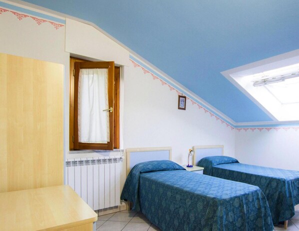 Une chambre avec deux lits, un radiateur, un bureau en bois et une fenêtre avec un rideau.