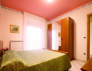 Une chambre à coucher avec un lit, un radiateur, une fenêtre avec des rideaux, un miroir et une porte.