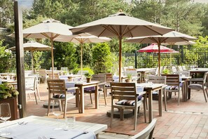 Une terrasse extérieure avec des tables et des chaises, des parasols et des plantes en pot.
