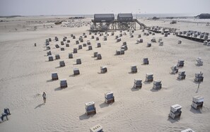 A beach with numerous beach chairs and umbrellas arranged in rows, a pier with buildings, and the ocean in the background. - Aalernhus Residenzen in St.peter-ording (St. Peter-Ording)