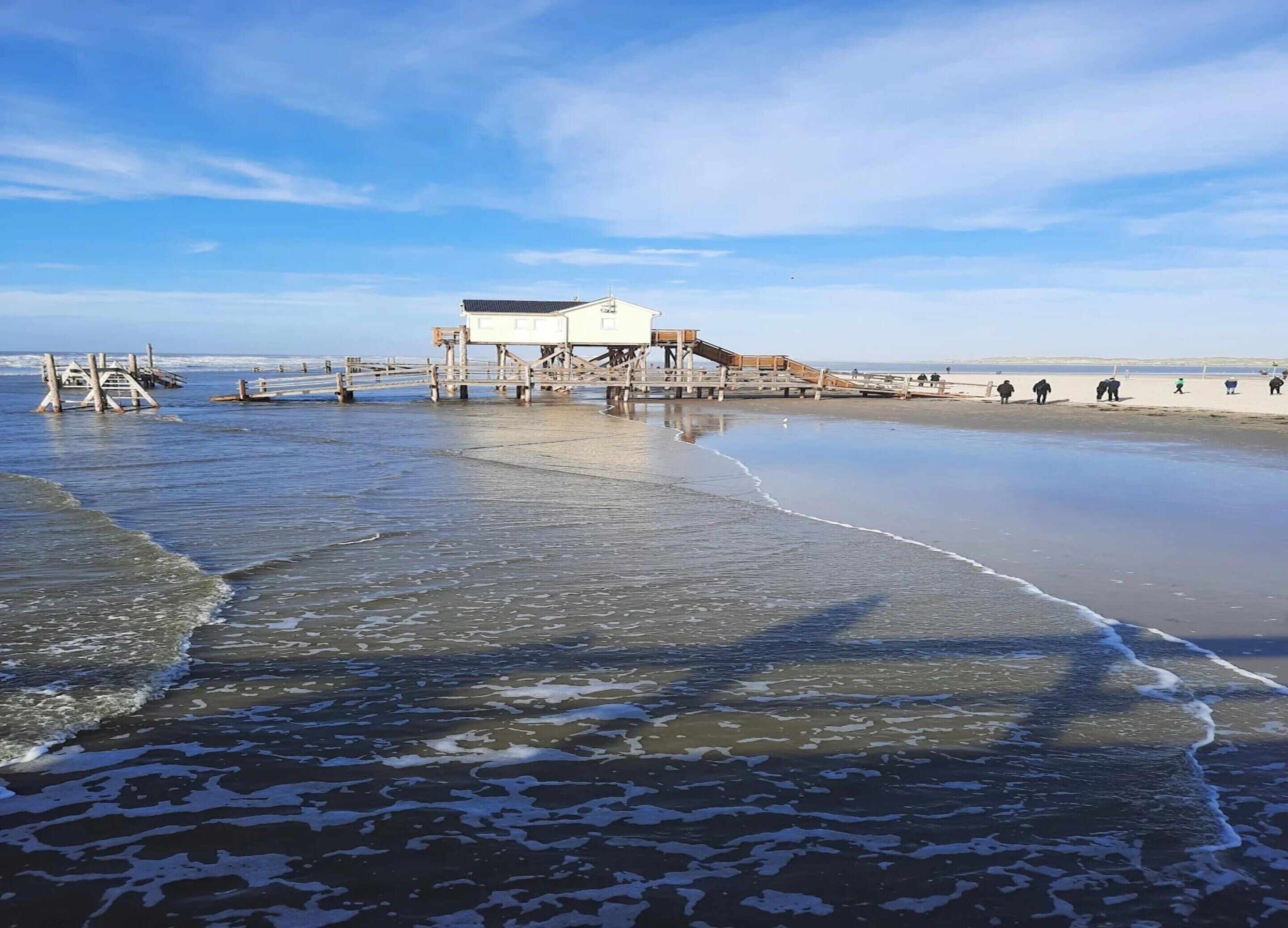 Una playa con un muelle de madera y un edificio blanco de techo plano.