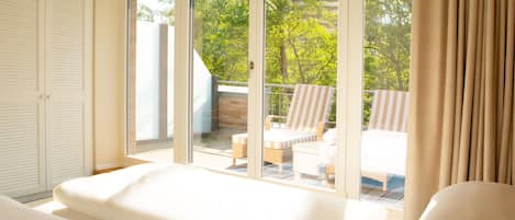 A bedroom with a large sliding glass door leading to a balcony with a view of trees and a building.