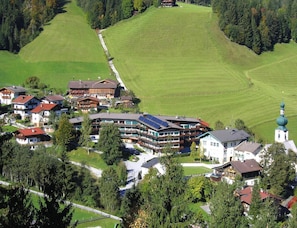 A multi-story hotel with a ski lift, surrounded by lush green fields and a church with a green dome. - Apartment in Wildschonau by Schatzberg Lift (Wildschönau)
