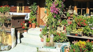 Un bâtiment en bois doté d’un porche, d’un escalier menant à l’entrée, ainsi que de diverses plantes et fleurs en pot.