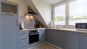 A modern kitchen with grey cabinets, a built-in oven, a coffee maker, and a microwave. - Ferienwohnung Kustenluft in Tating (Tating)