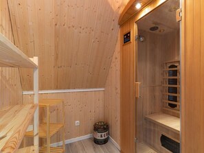 Sala de sauna de madera con un banco, una puerta y un estante pequeño con botellas.