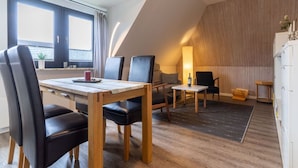 A modern, well-lit room with a dining table, chairs, a sofa, and a lamp. - Ferienwohnung Kustenluft in Tating (Tating)