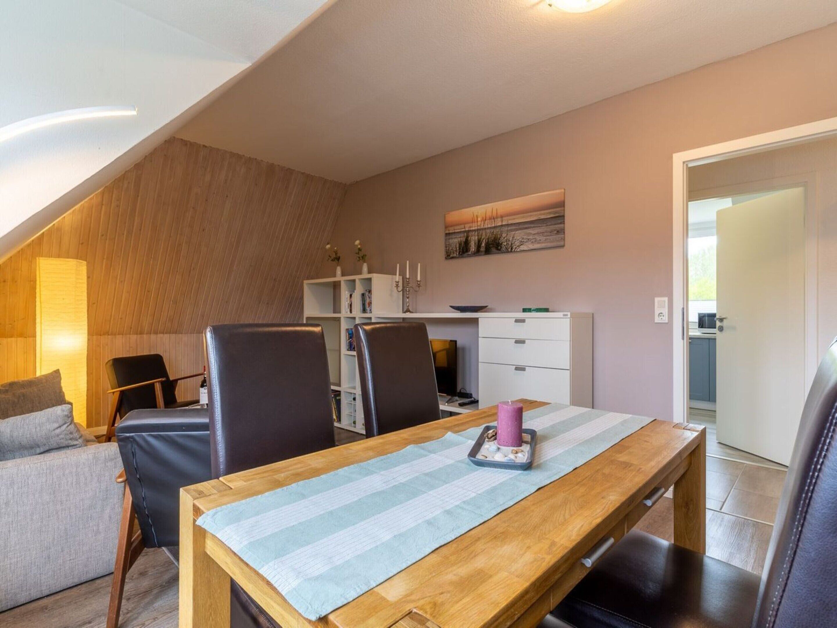 Un rincón comedor acogedor con una mesa de madera, mantel a rayas y sillas negras. Se aprecia en el fondo un estante con libros y velas.