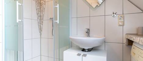 A modern bathroom with a glass shower enclosure, a white sink, and a washing machine.