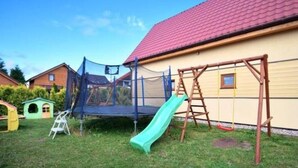 A backyard with a trampoline, a slide, a wooden swing set, and a small playhouse. - Holiday Studio Near the Beach, Sarbinowo (Mielno)