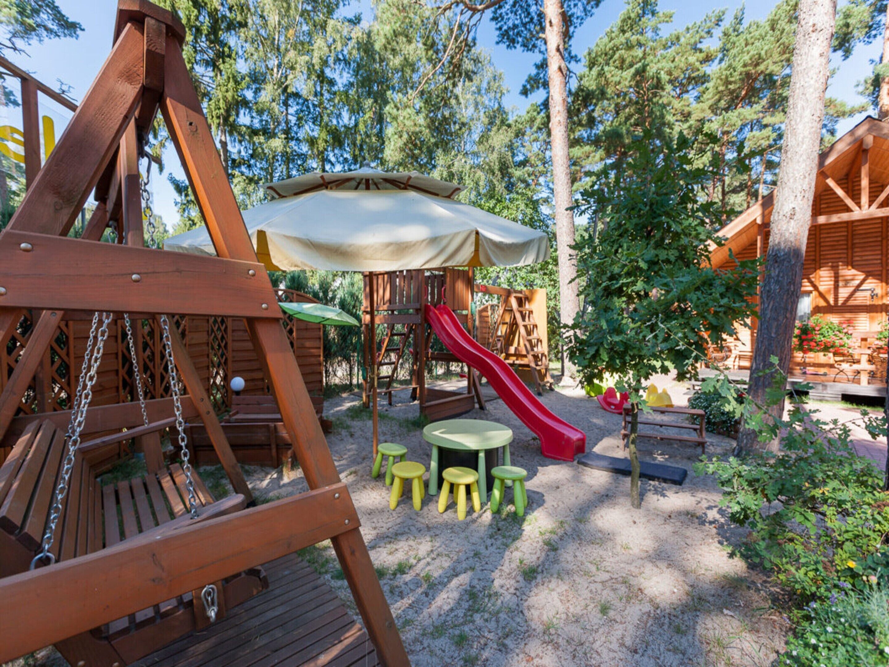 A wooden play structure with a slide, surrounded by trees and a picnic area.