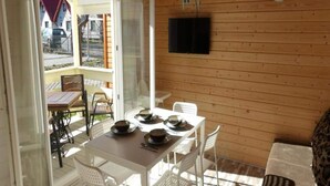 A wooden cabin with a dining area featuring a table and chairs, a television mounted on the wall, and a sliding glass door leading to an outdoor patio. - Holiday Homes With Terraces, Close to the Beach (Ustronie Morskie)