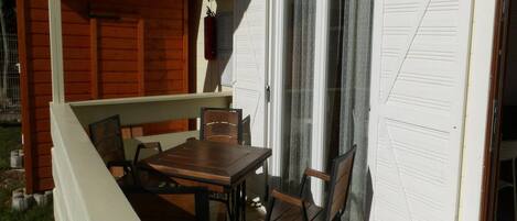 A patio with a wooden table and chairs, a sliding glass door, and a white exterior wall.